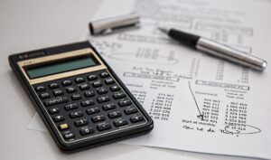 A calculator and pen on a paper - Bookkeeper vs. Accountant: Which is right for your business?